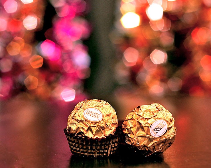 Dos bombones Ferrero Rocher encima de una mesa con luces al fondo